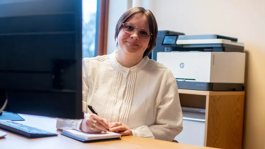 Smilende regnskapsfører i Flyd tar notater i en notatbok ved skrivebordet