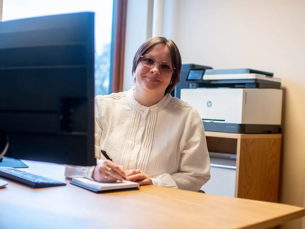 Smilende regnskapsfører med notatbok ved skrivebordet