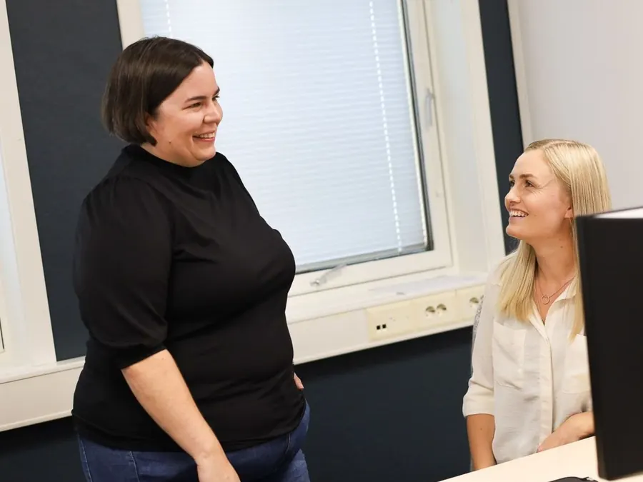To kolleger ler sammen ved en arbeidsplass på Moi-kontoret