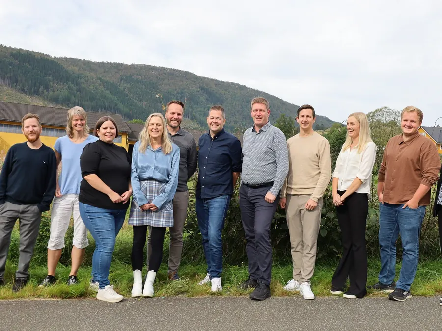 Flyd-kolleger på rad utendørs på Moi, med skogkledde åser og gule bygninger i bakgrunnen